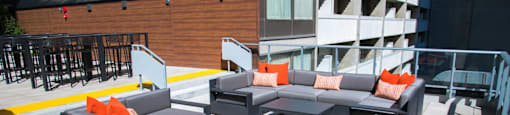 A grey couch with orange pillows is on a patio.