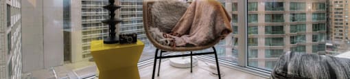 A chair with a brown blanket on it is in front of a window with a view of a city.