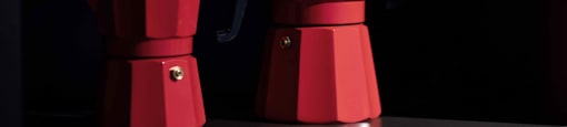 Two red coffee pots on a black surface.