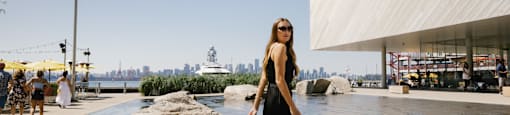 A woman in a black dress is walking by a body of water.