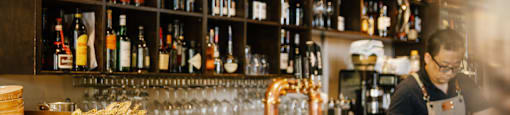 A bar with a man behind the counter and a shelf full of bottles.