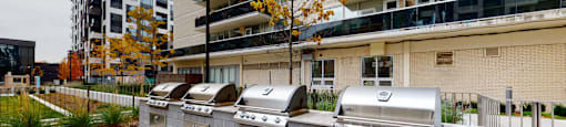 A row of outdoor grills are lined up on a brick patio.