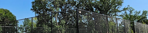 A tennis court is surrounded by a green fence and trees.