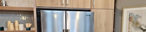 A stainless steel refrigerator with wooden cabinets and a trash can in a kitchen.