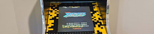 A small arcade machine with a black background and yellow and black pixelated design.