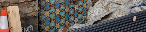 A door with a pattern of blue and orange diamonds is set in a brick wall.