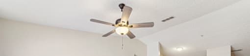 an empty living room with a ceiling fan and a kitchen