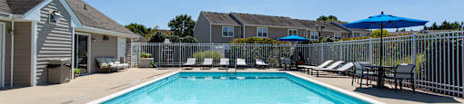 A swimming pool surrounded by a white fence and blue umbrellas.