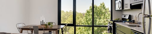 A modern kitchen with a dining table and a couch with a view of trees outside.
