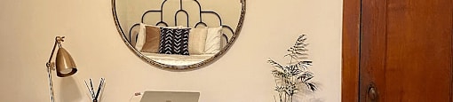 a home office with a desk and a mirror and plants on the wall