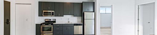 A modern kitchen with dark grey cabinets and a wooden floor.