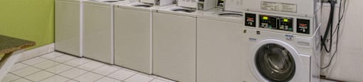 a row of washers and dryers in a laundry room with washing machines