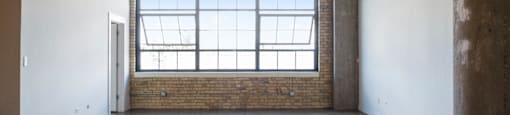 an empty room with a window and concrete floors and a brick wall