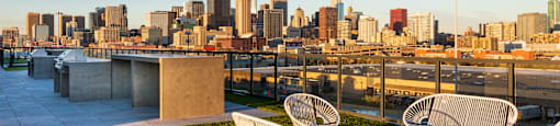 Three white chairs are on a patio overlooking a city skyline.