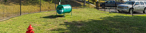 A green barrel sits on a grassy area next to a red fire hydrant.