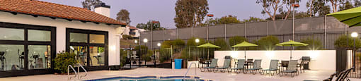 A pool with sun loungers and umbrellas in front of a building.