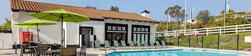 A pool with a ladder and a table with chairs and an umbrella outside a building.