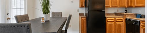 A black fridge sits in a kitchen with wooden cabinets.