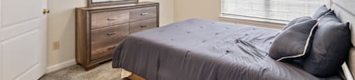 A bedroom with a bed, dresser, and window.