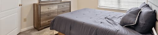 A bedroom with a bed, dresser, and window.