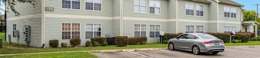 A silver car is parked in front of a grey apartment building.