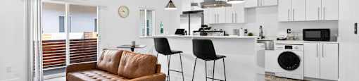A modern kitchen with a brown leather sofa and black bar stools.