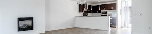 an empty living room with a fireplace and a kitchen
