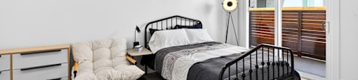 A bedroom with a black metal bed and a white chair with a wooden frame.