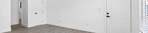 A room with white walls and wooden flooring with two doors.