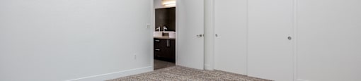 a bedroom with white walls and carpet and doors to a bathroom