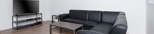 A black leather sofa sits in a room with a ceiling fan and a television.