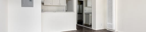 an empty living room and kitchen with white walls and wood flooring
