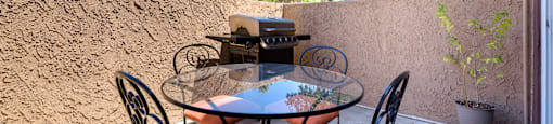 a patio with a glass table and chairs and a grill