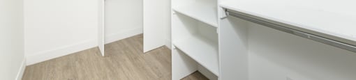 a walk in closet with white walls and shelves and a wood floor