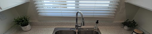 A kitchen sink with a faucet and a window with blinds.