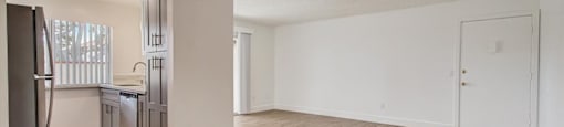 an empty living room with a kitchen in the background