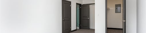an empty living room with white walls and grey carpet and two doors to different rooms