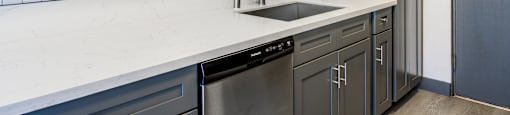 an empty kitchen with white countertops and a stainless steel sink