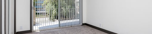 an empty living room with a sliding glass door to a balcony