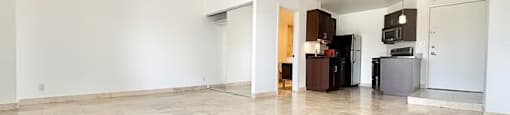 A spacious room with tiled flooring and a kitchen area in the background.