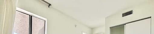 A white tiled room with a window, a door, and a wall-mounted air vent.