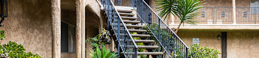 a staircase with a black railing and green plants in front of it
