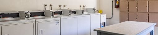 a row of washers and dryers in a room with a table in the foreground