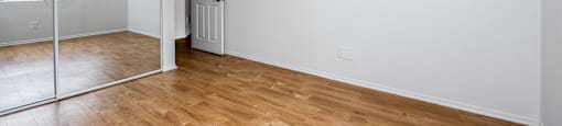 the living room and bedroom of an apartment with wood flooring and a mirrored closet
