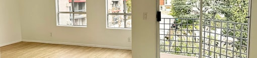 A room with a sliding glass door leading to a balcony with a view of a tree and a building.