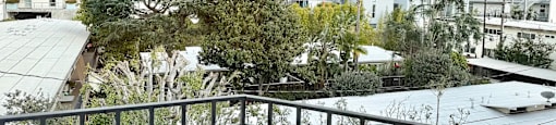 A balcony with a metal railing overlooks a courtyard with potted plants and trees.