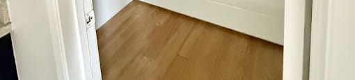 A white door is open to a room with wooden floors and white walls.