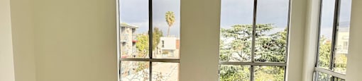 A room with wooden flooring and two windows overlooking a residential area.