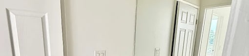 A white door is on the left of a bathroom with a marble countertop and a mirror.