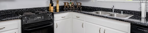 a kitchen with white cabinets and black counter tops and black appliances